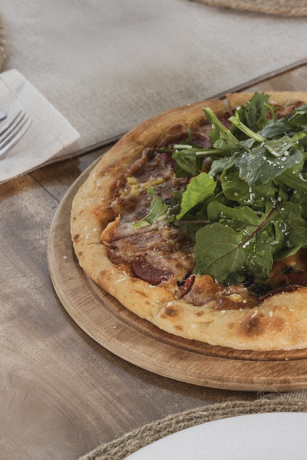 Taş fırından çıkan, roka ve rendelenmiş peynirle servis edilen pizza