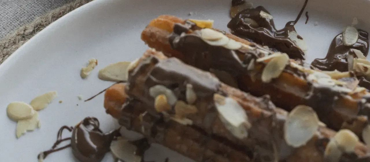 Churros with chocolate sauce and sliced almonds, dipped into warm chocolate cream